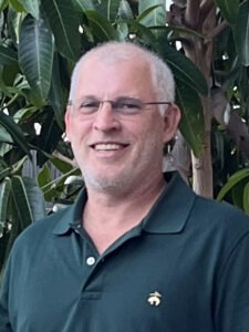 a man in a green shirt standing in front of a tree