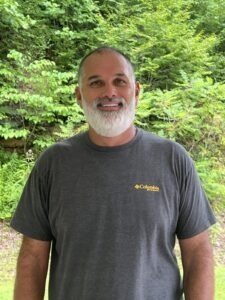 a man standing in front of a lush green forest