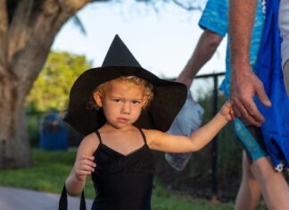 a little girl in a witches costume walking down the street