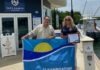 CLEAN MARINAS, CLEAN WATERS: VOLUNTARY INITIATIVE ESTABLISHES ENVIRONMENTAL PRACTICES a man and a woman holding a blue and yellow flag