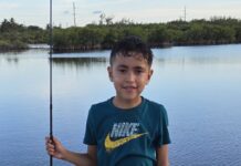 a young boy holding a fishing pole in front of a body of water