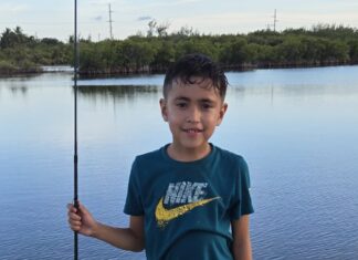 a young boy holding a fishing pole in front of a body of water