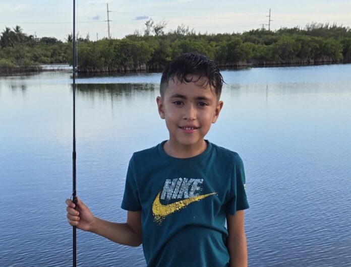 a young boy holding a fishing pole in front of a body of water