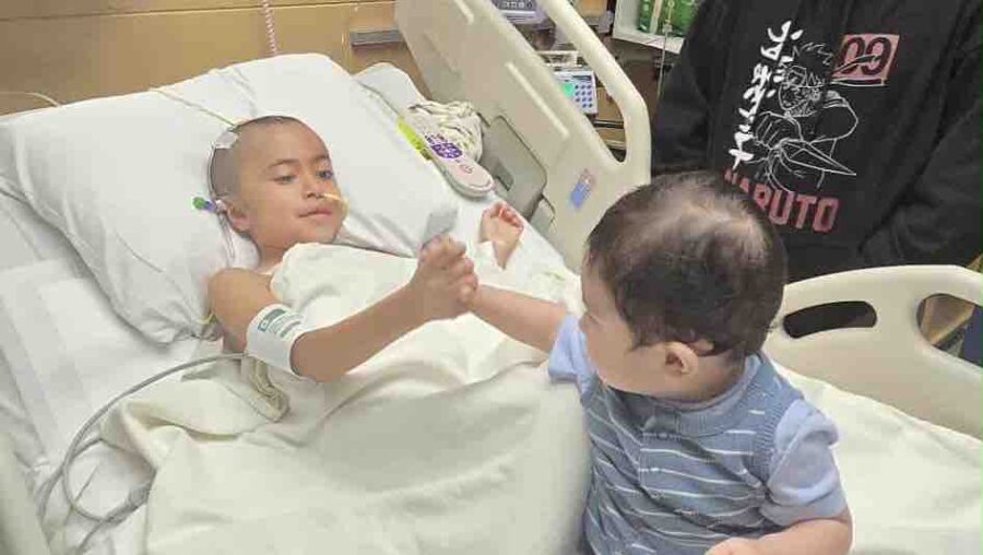 a little boy laying in a hospital bed next to an adult