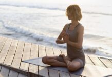a woman sitting on a yoga mat in front of the ocean