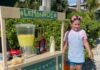 a little girl standing in front of a lemonade stand