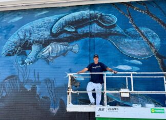 MURAL GETS A MANATEE: WYLAND ADDS TO ICONIC WHALING WALL AT SURFSTYLE a man standing on a ladder in front of a mural