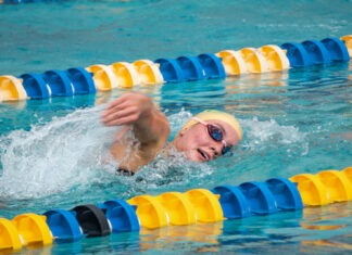 CORAL SHORES’ LYKINS & SMITH PUNCH TICKETS TO STATES IN THE POOL a man swimming in a pool with a yellow hat