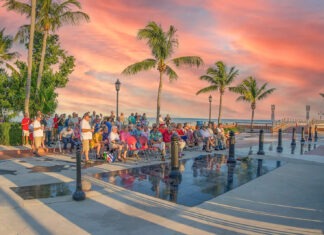 a crowd of people standing around a pool at sunset