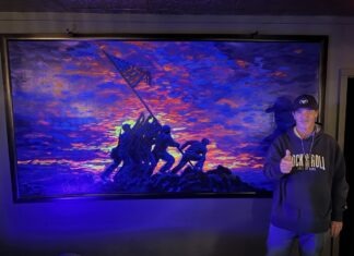 RENOWNED ARTIST UNVEILS ‘RAISING THE FLAG’ AT THE ARMORY SPEAKEASY IN KEY LARGO a man standing in front of a painting