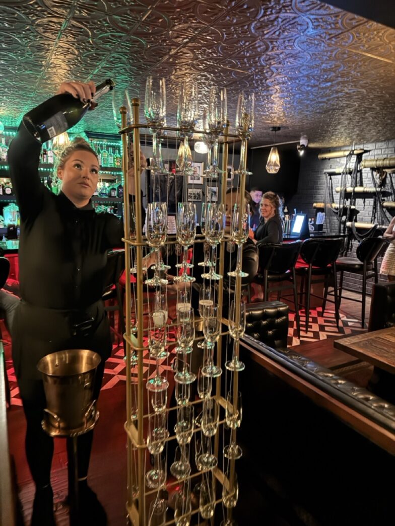 a man standing next to a tall metal rack filled with wine glasses