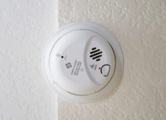 SMOKE ALARMS SAVE LIVES; AND DON’T FORGET TO CHANGE OUT THE BATTERIES a white smoke detector mounted on a wall