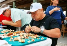 LOCALS TAKE TOP MARKS IN KEYS FISHERIES STONE CRAB EATING CONTEST a group of people standing around a table with food on it