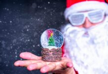 Festive image of a Santa figure holding a snow globe with a Christmas tree.