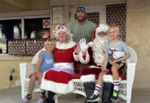 SNAPS WITH SANTA: NORTH POLE’S LEADING COUPLE VISIT COLDWELL BANKER SCHMITT a man sitting on a chair with two children and a santa clause