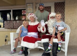 SNAPS WITH SANTA: NORTH POLE’S LEADING COUPLE VISIT COLDWELL BANKER SCHMITT a man sitting on a chair with two children and a santa clause