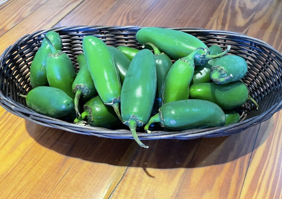 a basket filled with green peppers on top of a wooden table