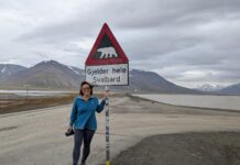 a woman standing next to a sign on the side of a road