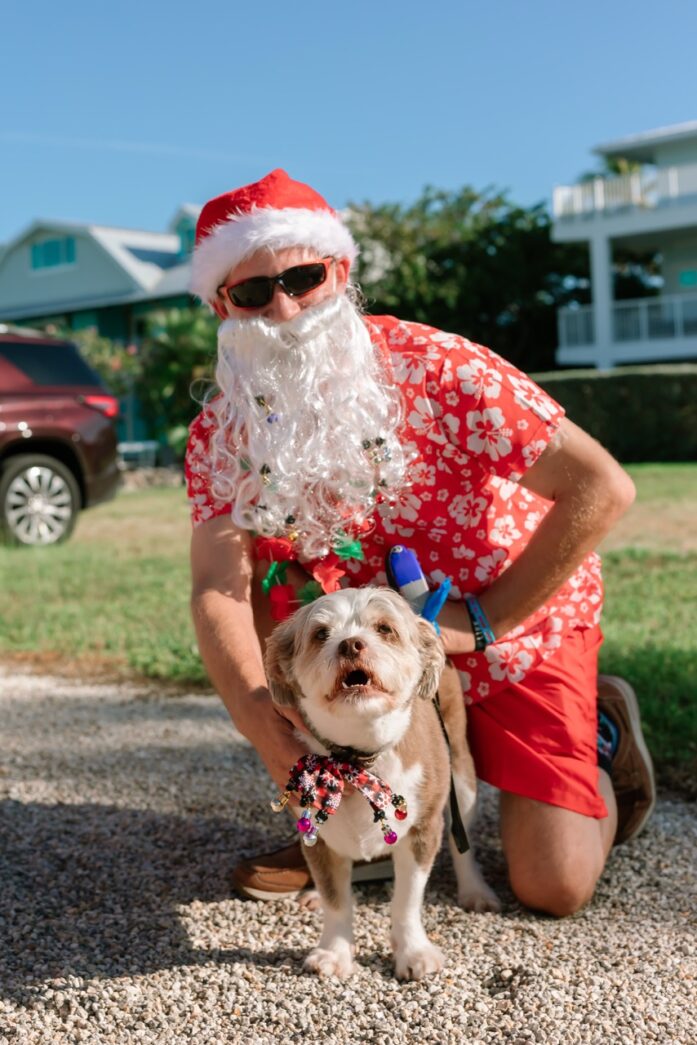 a man with a beard and a santa clause hat kneeling down next to a dog