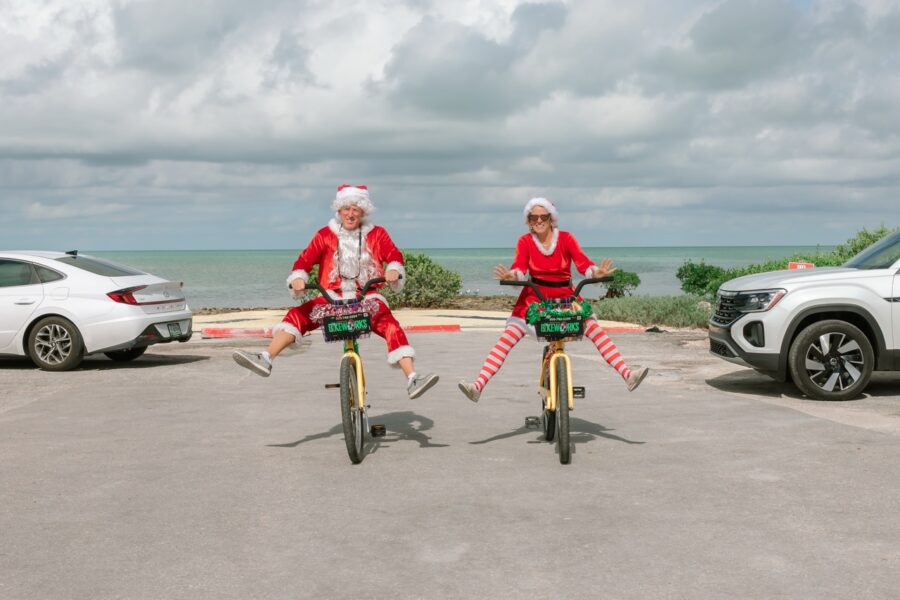 two people dressed as santa clause riding bikes in a parking lot