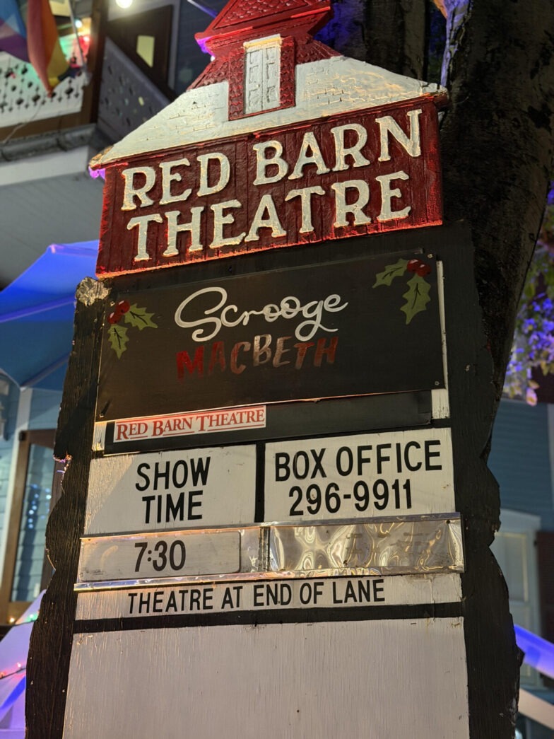 a red barn theatre sign in front of a tree