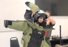 a man in a green jacket is holding a helmet on his head