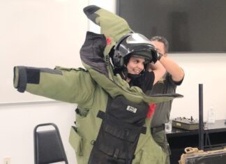 a man in a green jacket is holding a helmet on his head