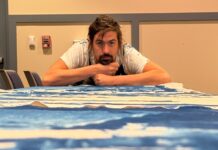 MARATHON CITY HALL’S NEWEST ART GALLERY REFRAMES HISTORY IN ROYAL BLUE a man sitting at a table with his arms crossed