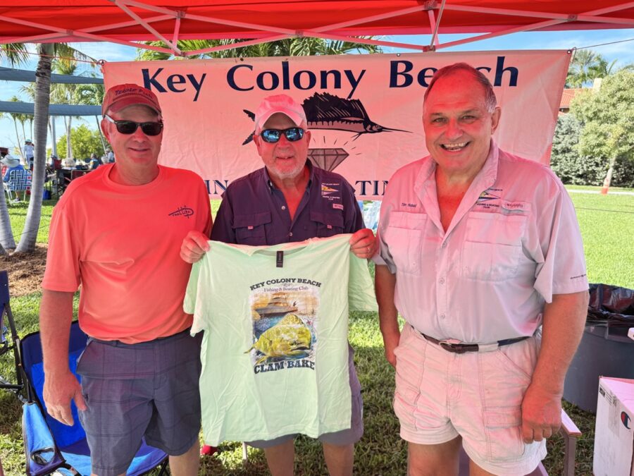 three men standing under a tent holding up a shirt