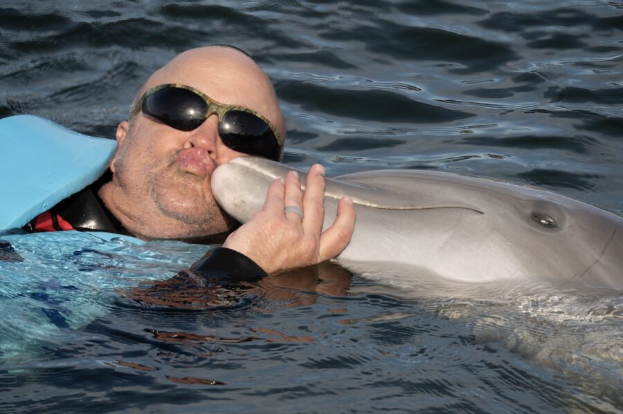 a man in sunglasses and a life jacket kissing a dolphin