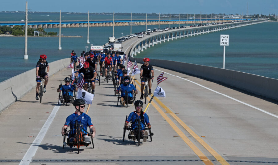 a group of people riding bikes down a road next to the ocean