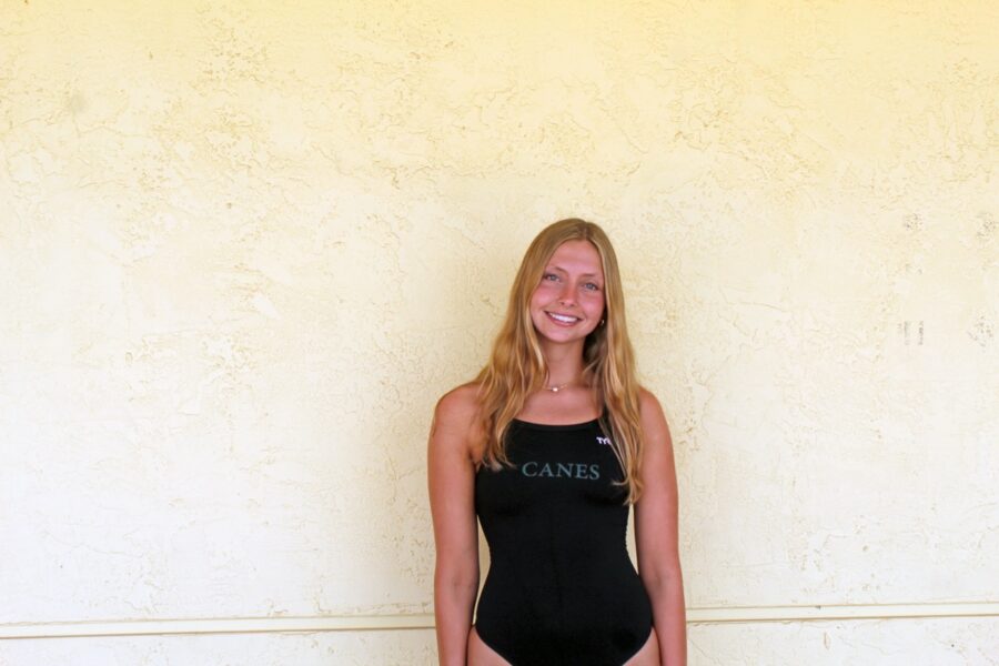 a woman standing in front of a wall wearing a black one piece swimsuit